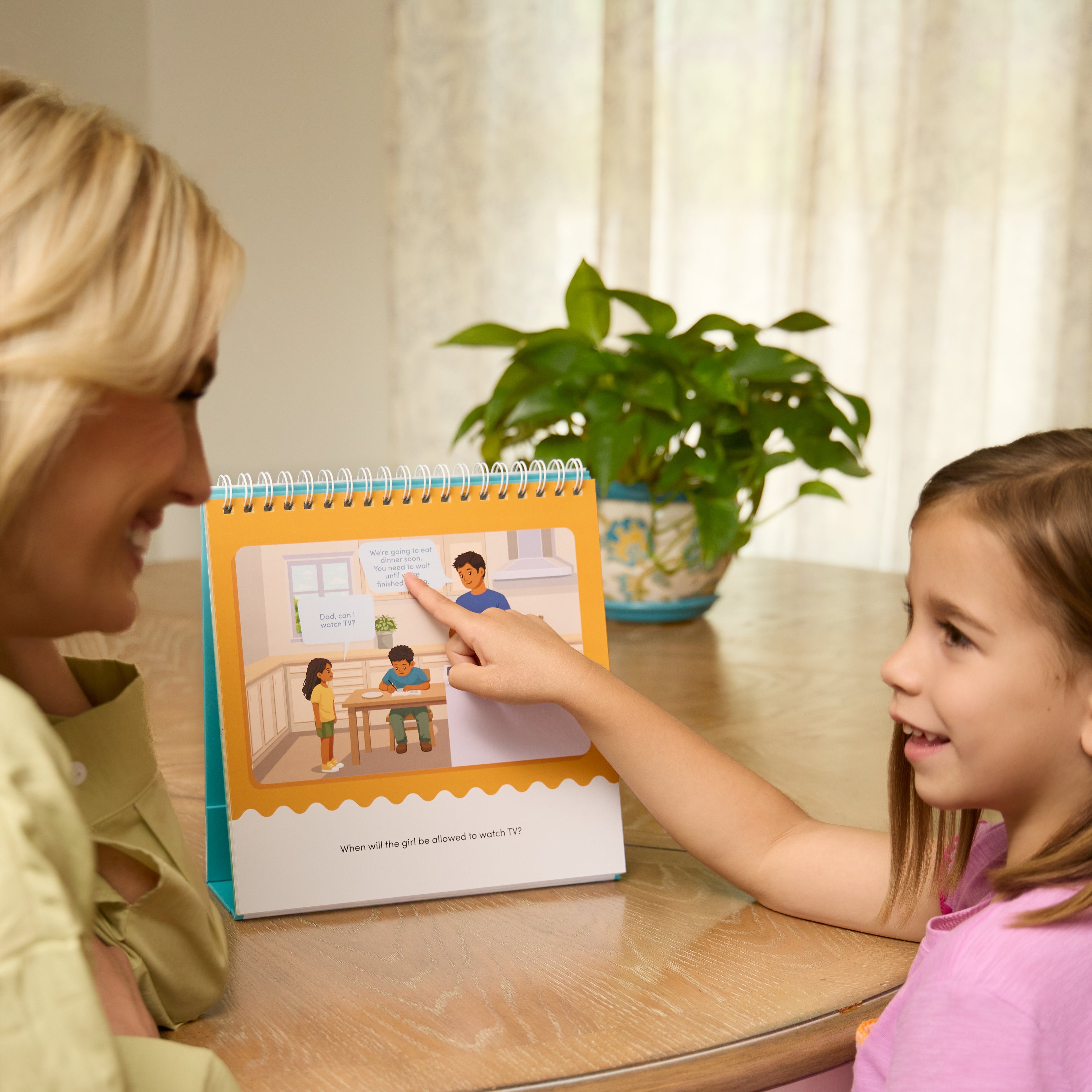 Woman and child looking at the Waiting for Things We Want book together on a table with a plant in the background