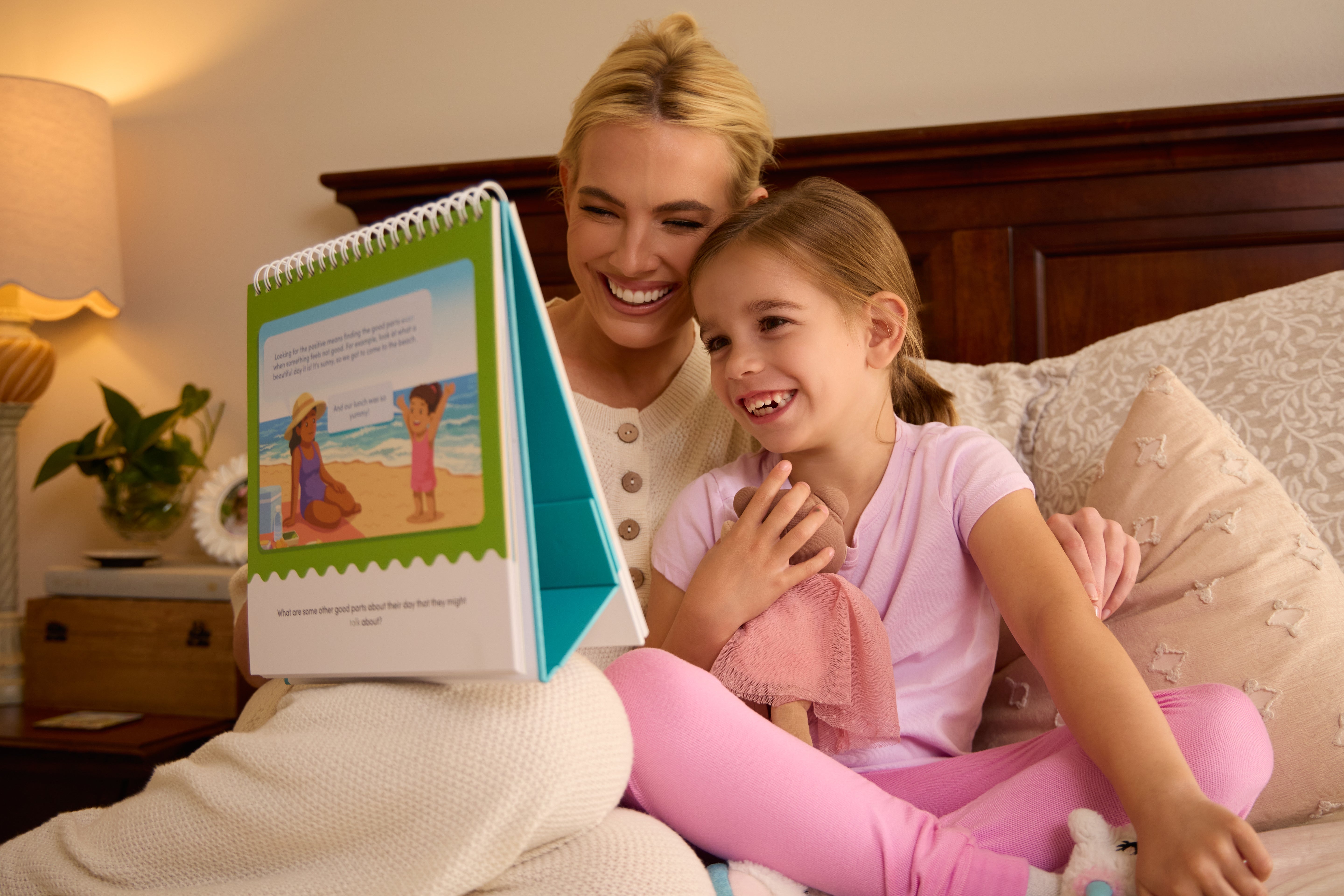 Woman and young girl sitting on a bed reading a book together.
